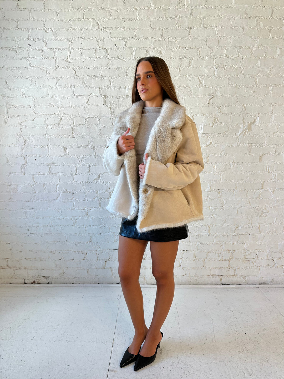 Woman wearing taupe reversible coat with one side being a faux fur, and the other side being suede. 