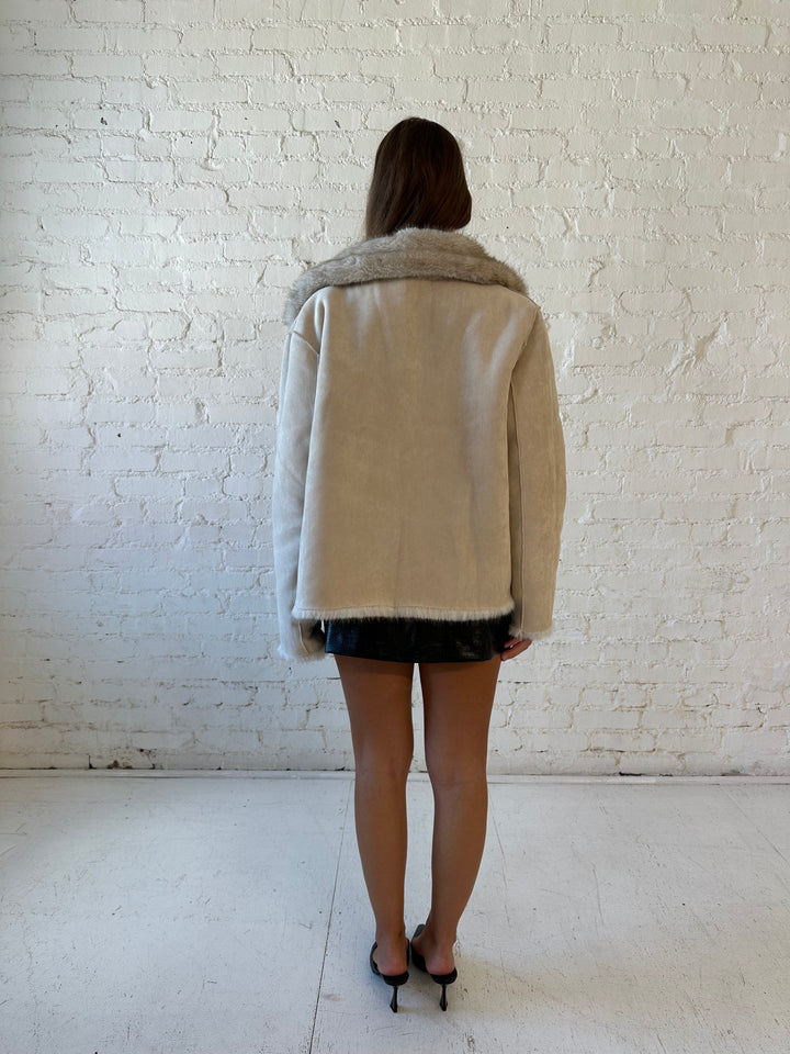Woman wearing taupe reversible coat with one side being a faux fur, and the other side being suede. 