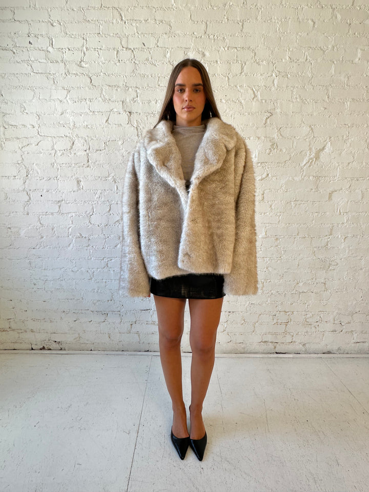 Woman wearing taupe reversible coat with one side being a faux fur, and the other side being suede. 
