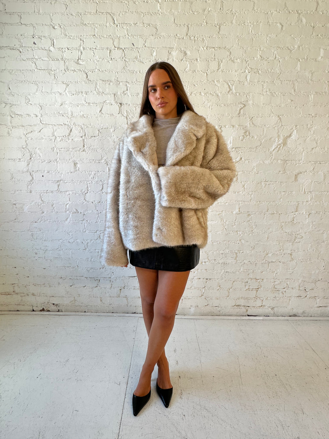 Woman wearing taupe reversible coat with one side being a faux fur, and the other side being suede. 