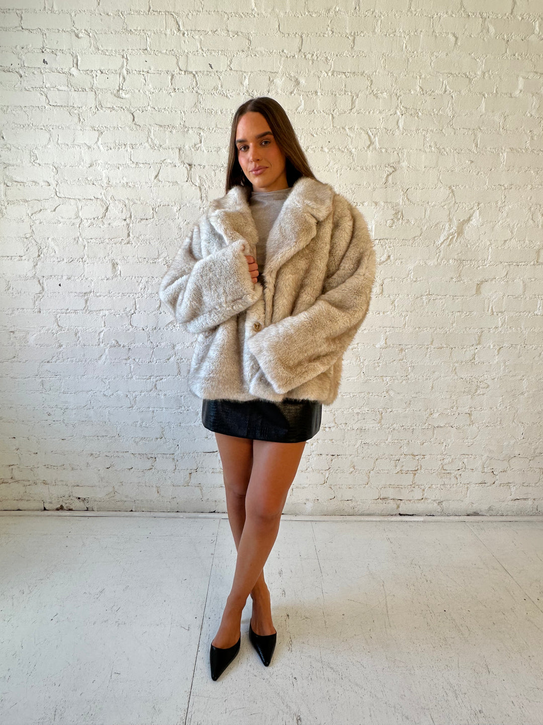 Woman wearing taupe reversible coat with one side being a faux fur, and the other side being suede. 