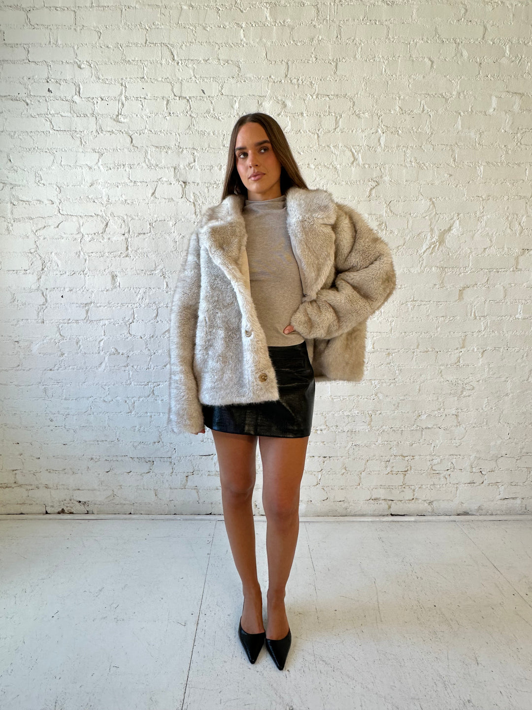 Woman wearing taupe reversible coat with one side being a faux fur, and the other side being suede. 
