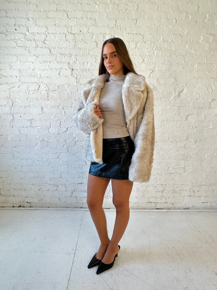 Woman wearing taupe reversible coat with one side being a faux fur, and the other side being suede. 