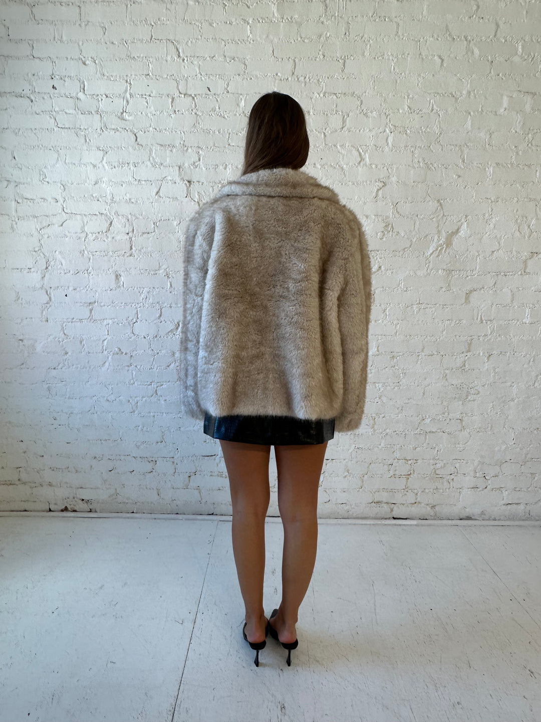 Woman wearing taupe reversible coat with one side being a faux fur, and the other side being suede. 
