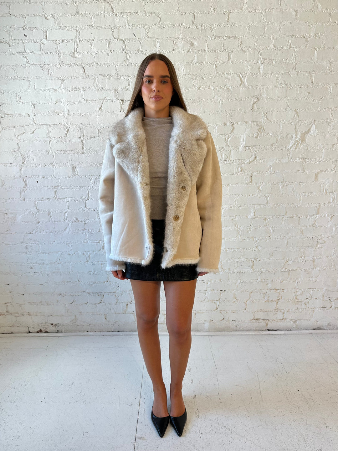 Woman wearing taupe reversible coat with one side being a faux fur, and the other side being suede. 