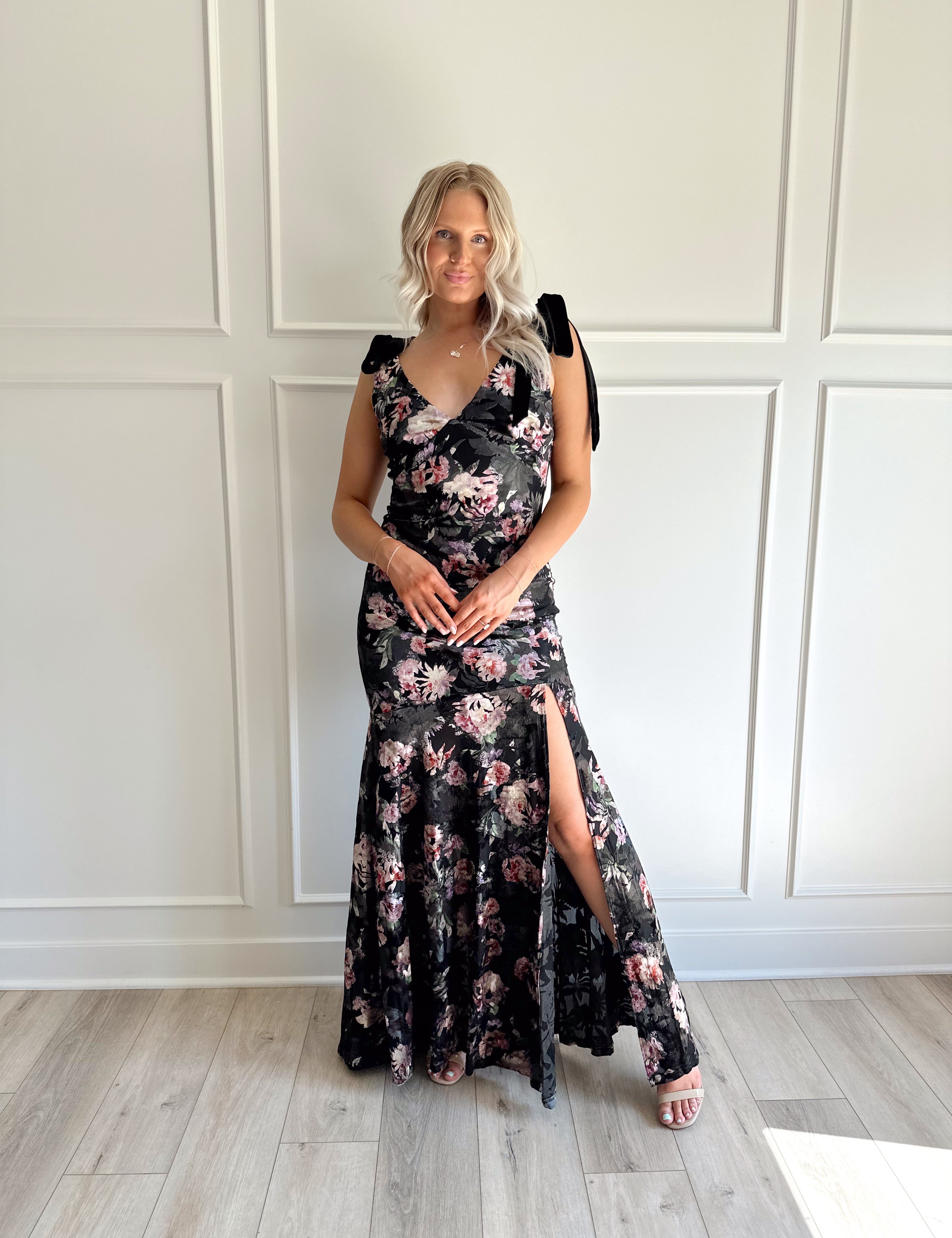 Woman wearing black velvet floral maxi dress with thigh-high slit and bow straps