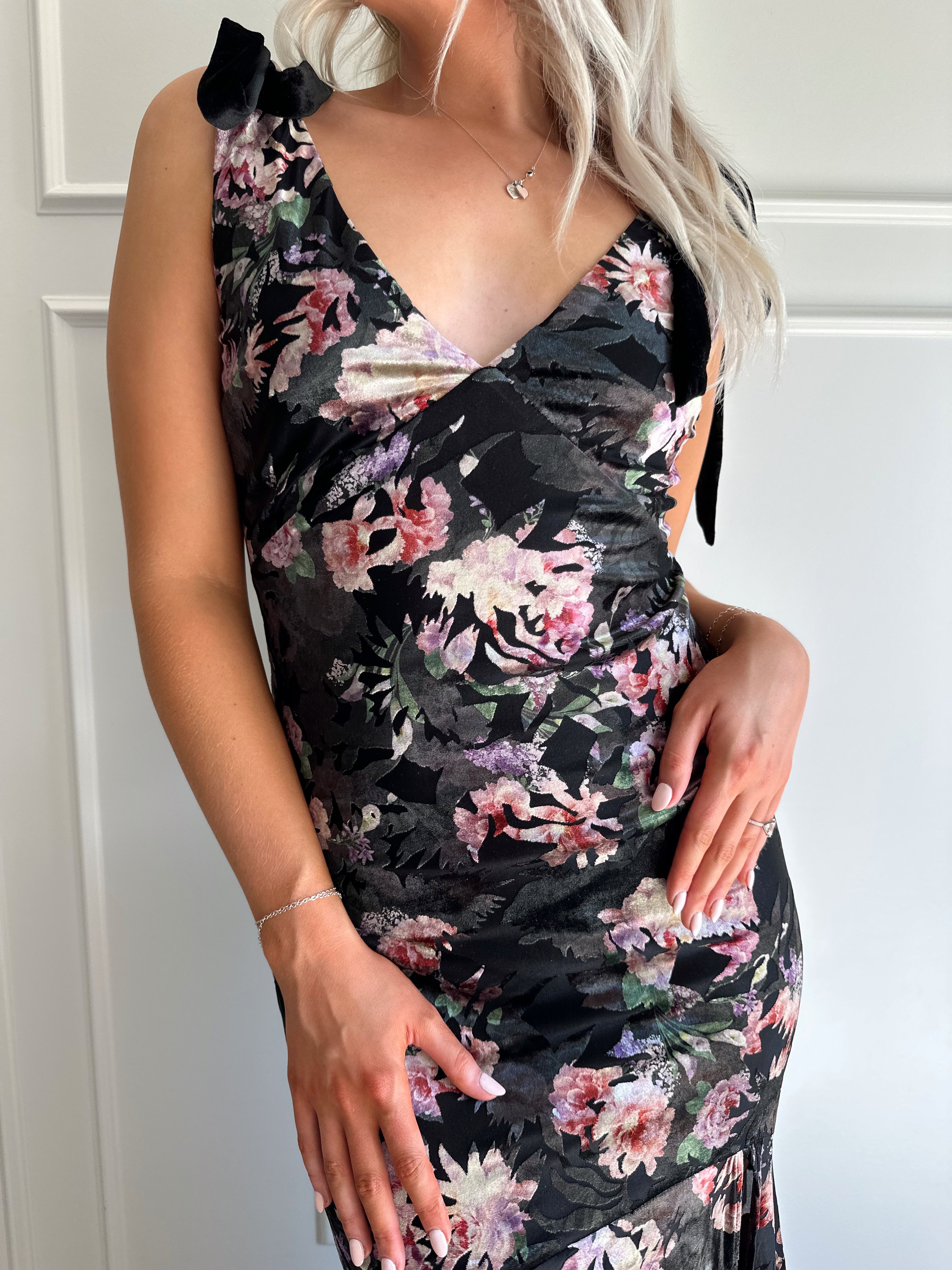 Woman wearing black velvet floral maxi dress with thigh-high slit and bow straps
