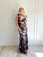 Woman wearing black velvet floral maxi dress with thigh-high slit and bow straps