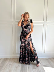 Woman wearing black velvet floral maxi dress with thigh-high slit and bow straps