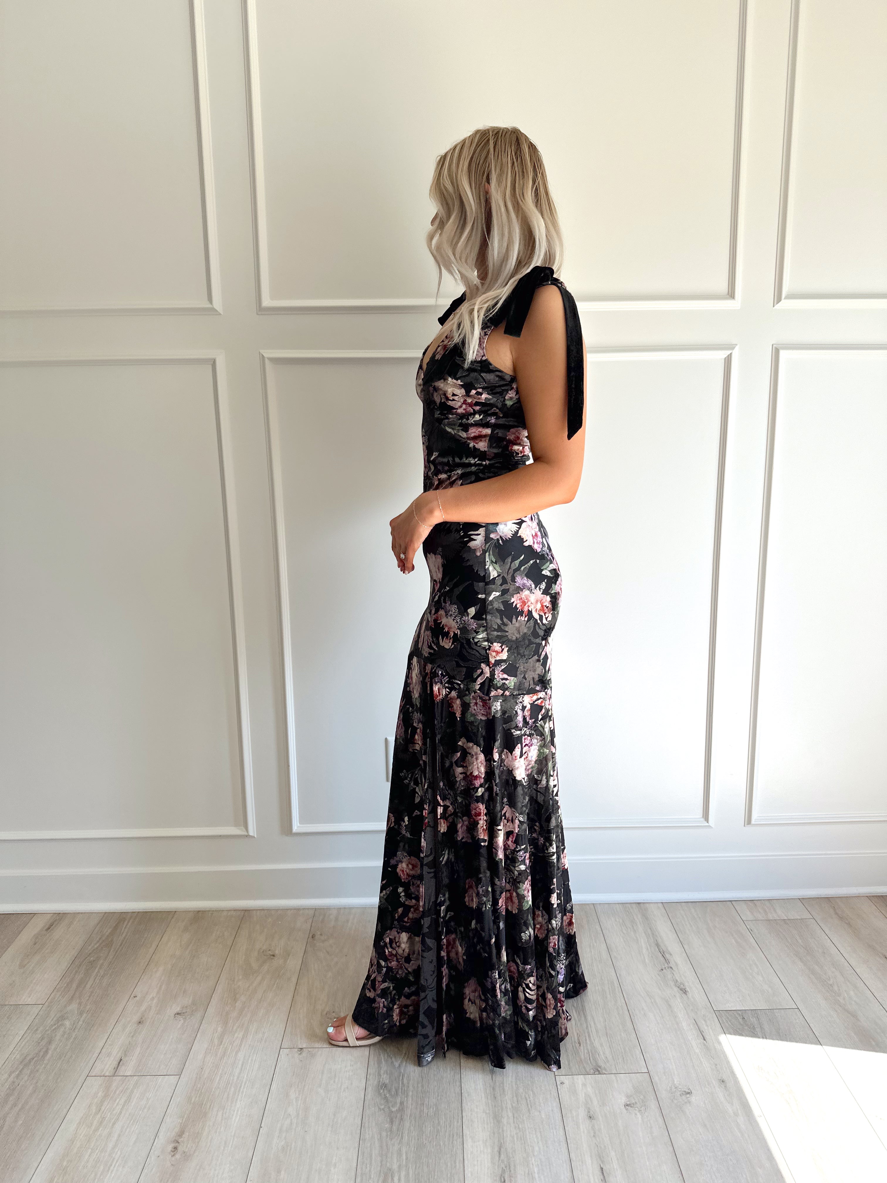 Woman wearing black velvet floral maxi dress with thigh-high slit and bow straps