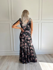 Woman wearing black velvet floral maxi dress with thigh-high slit and bow straps
