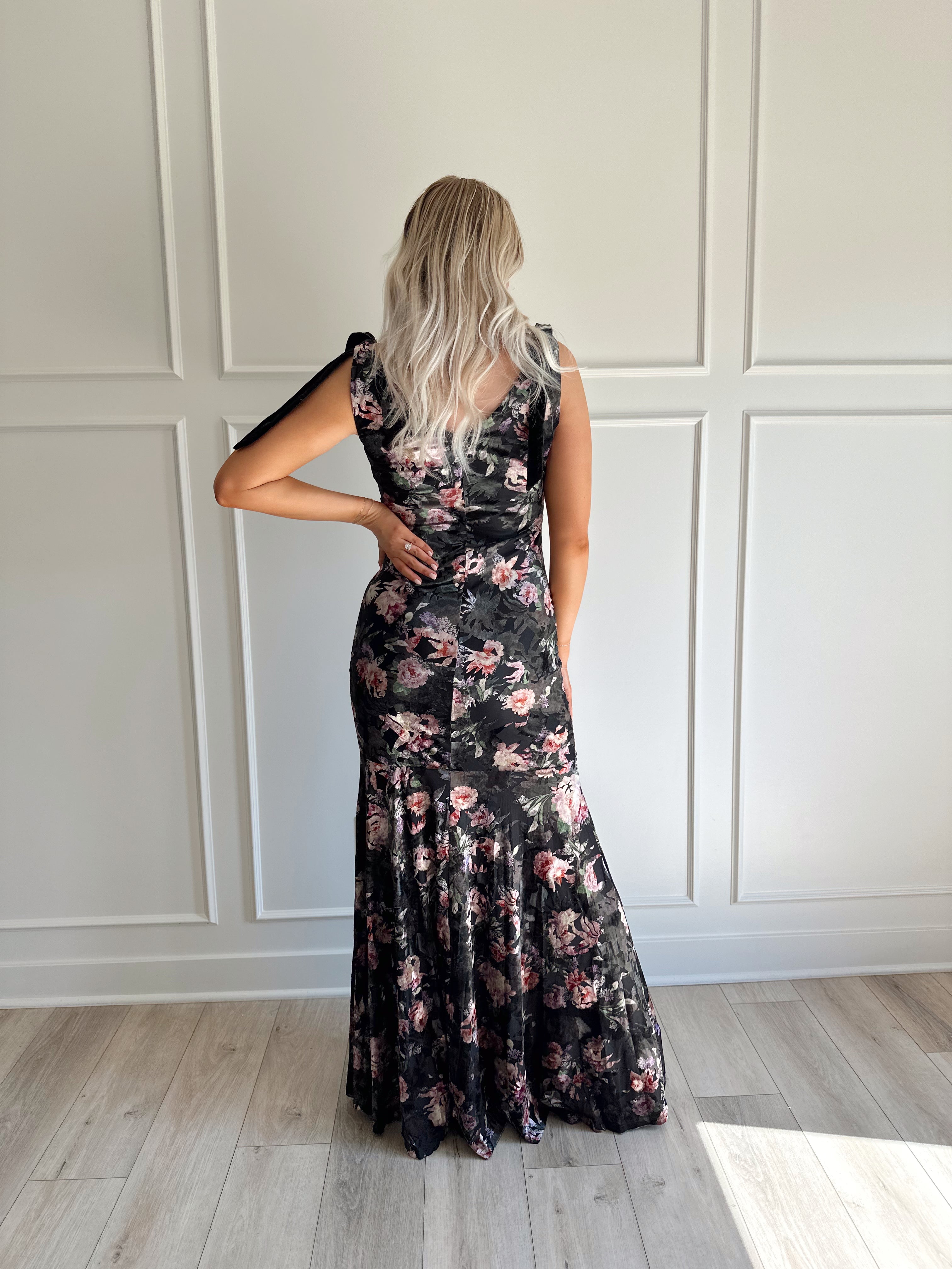 Woman wearing black velvet floral maxi dress with thigh-high slit and bow straps