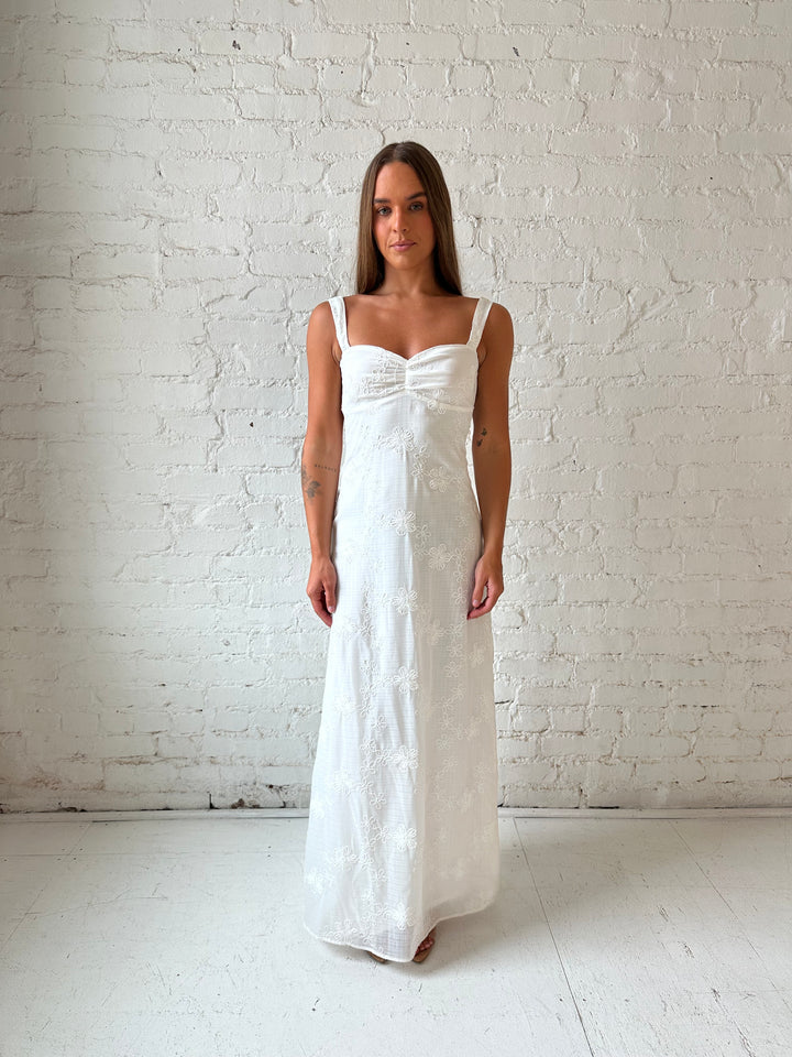 Woman wearing white embroidered maxi dress with sweetheart neckline, and tie back.