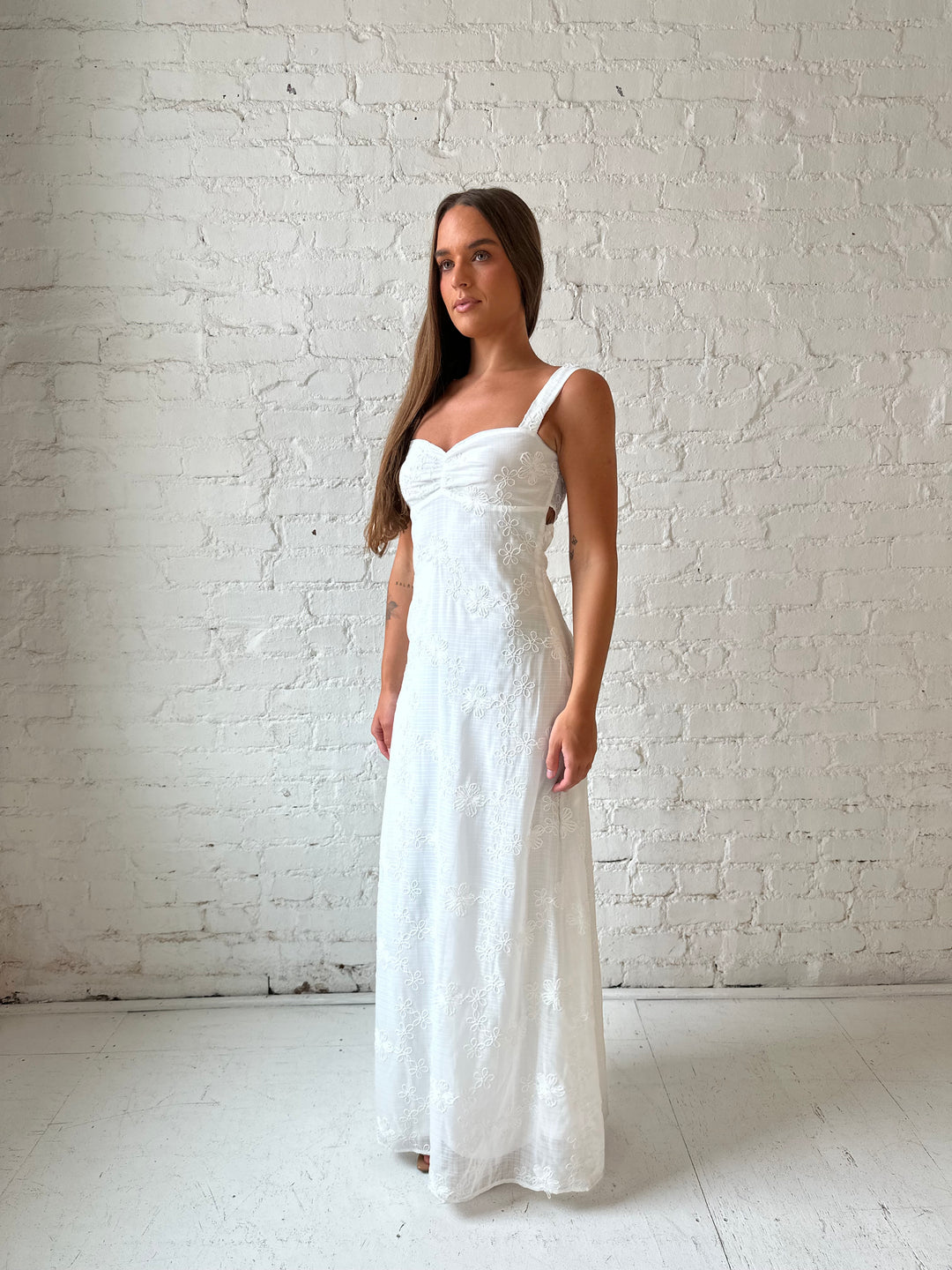Woman wearing white embroidered maxi dress with sweetheart neckline, and tie back.