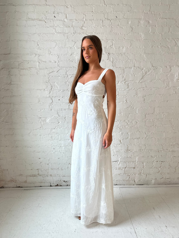 Woman wearing white embroidered maxi dress with sweetheart neckline, and tie back.