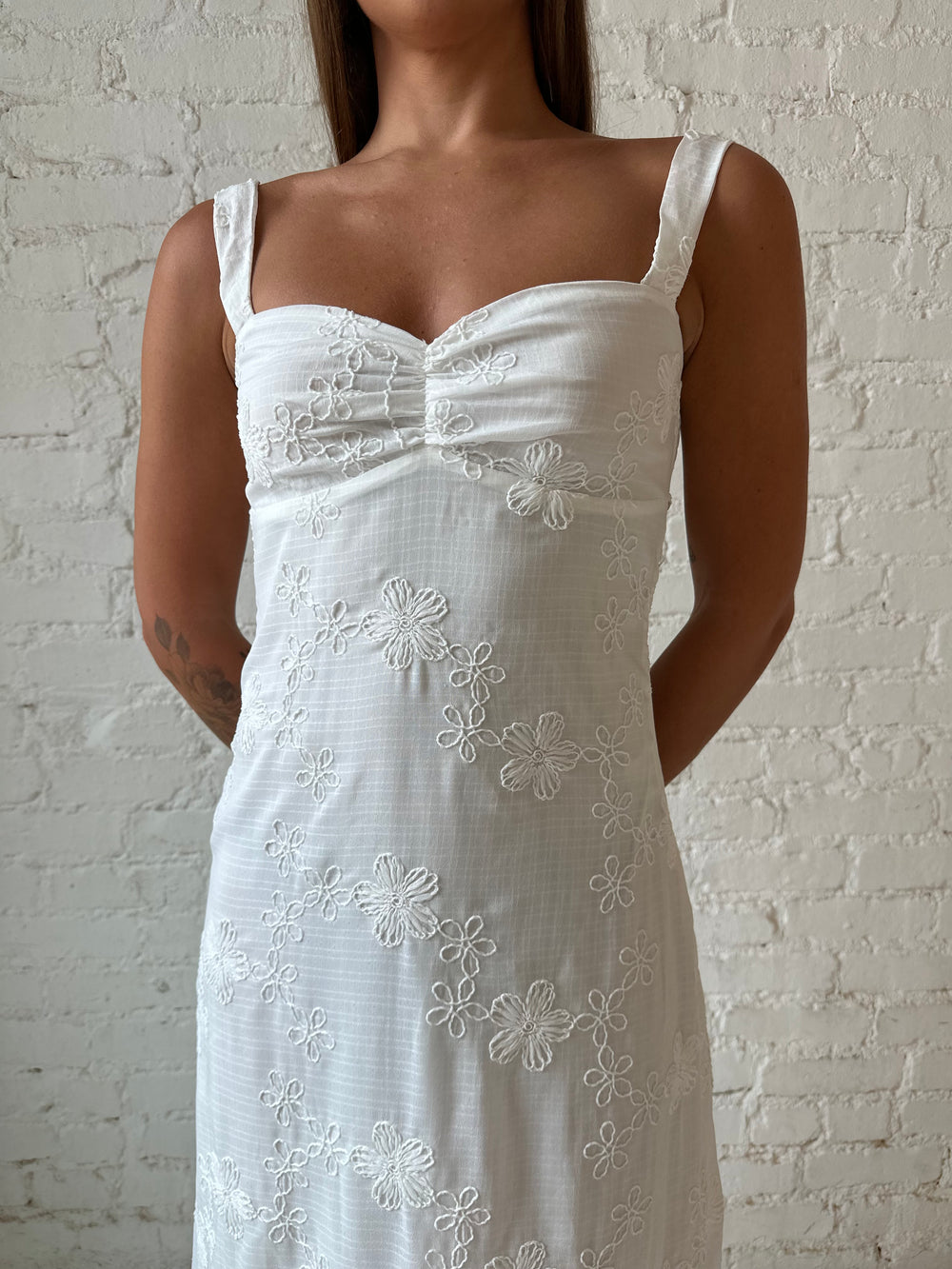 Woman wearing white embroidered maxi dress with sweetheart neckline, and tie back.