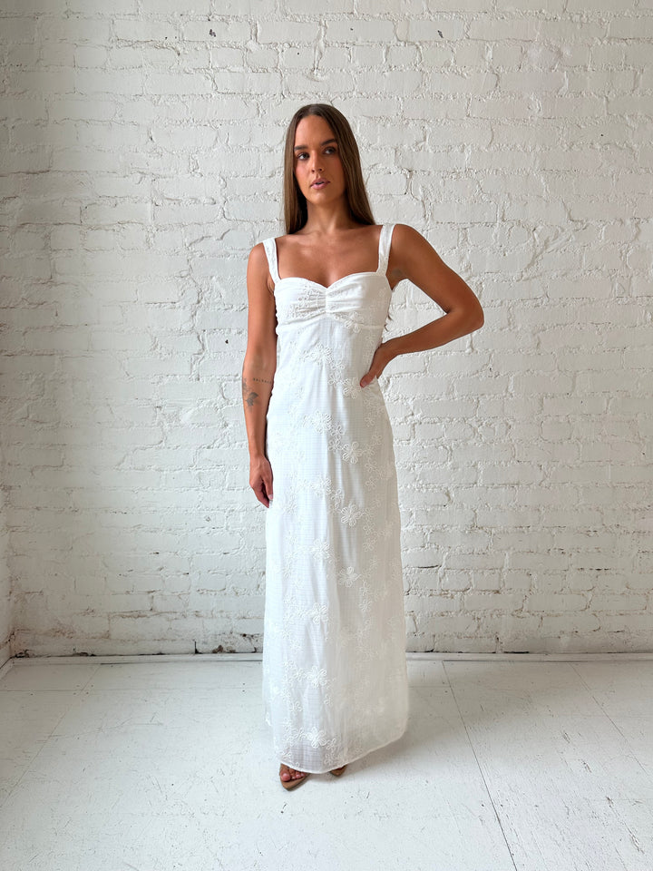 Woman wearing white embroidered maxi dress with sweetheart neckline, and tie back.