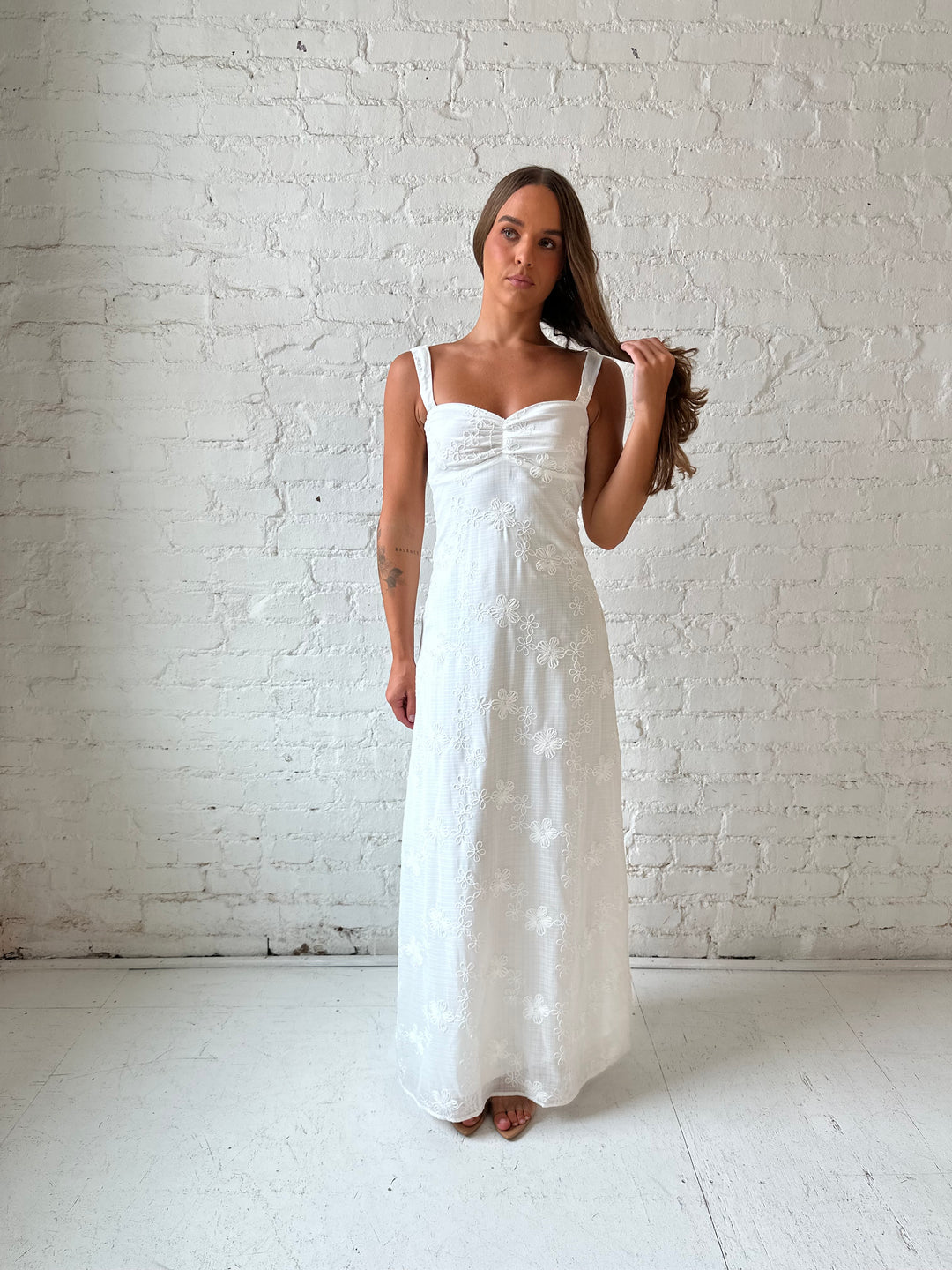 Woman wearing white embroidered maxi dress with sweetheart neckline, and tie back.