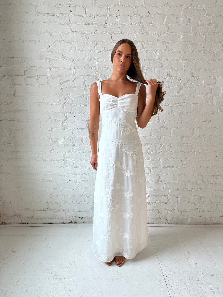 Woman wearing white embroidered maxi dress with sweetheart neckline, and tie back.