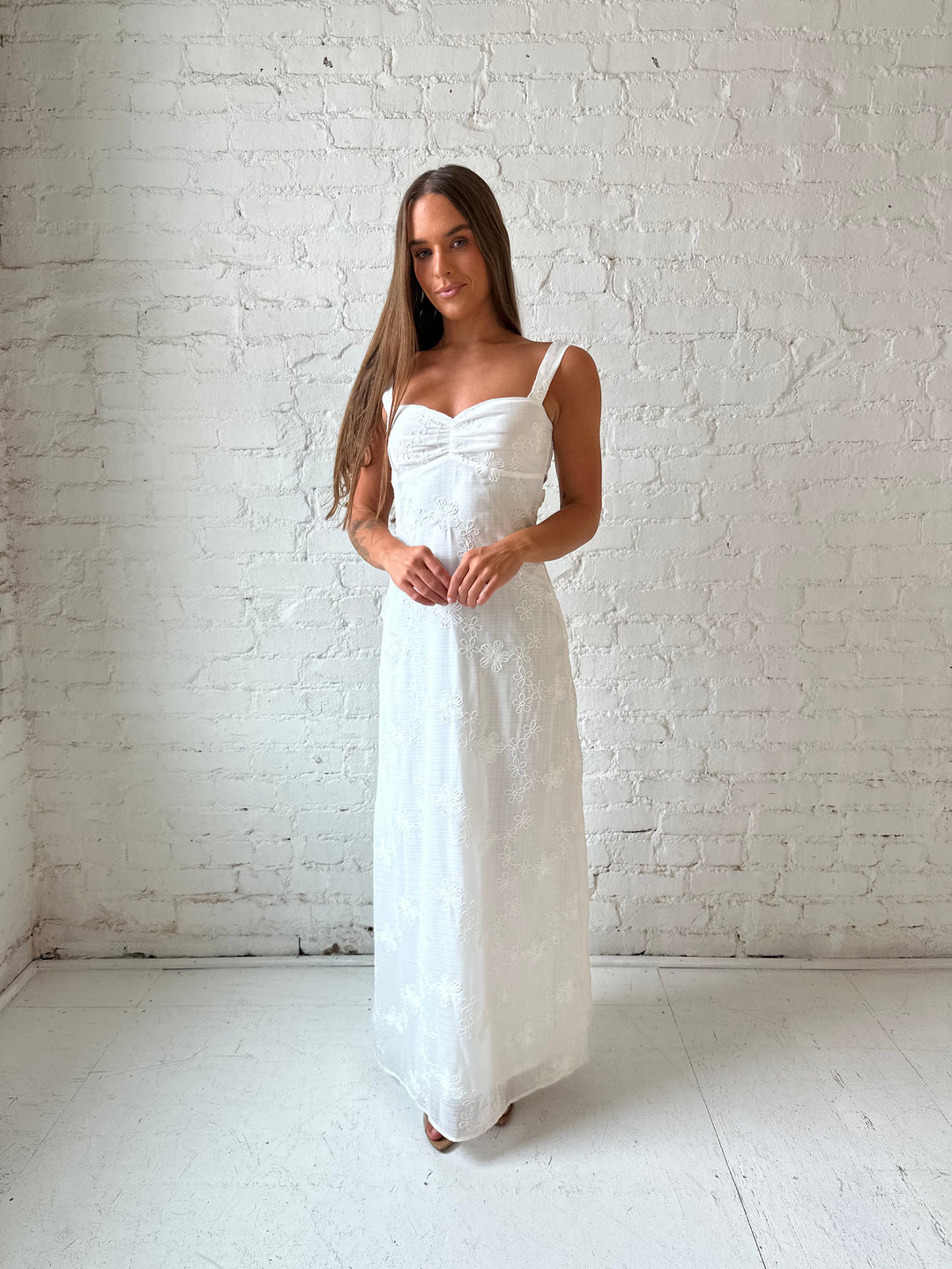Woman wearing white embroidered maxi dress with sweetheart neckline, and tie back.