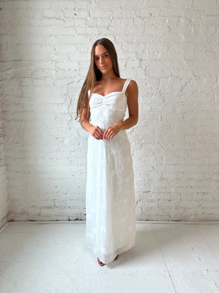 Woman wearing white embroidered maxi dress with sweetheart neckline, and tie back.