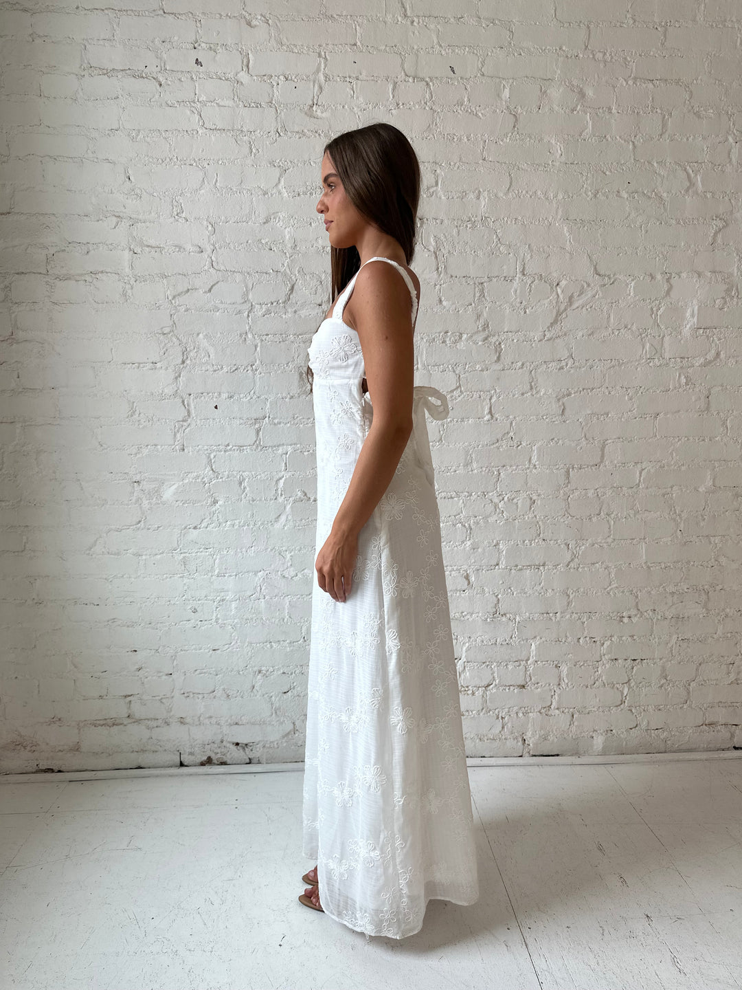 Woman wearing white embroidered maxi dress with sweetheart neckline, and tie back.