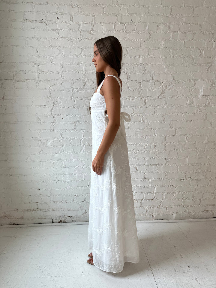 Woman wearing white embroidered maxi dress with sweetheart neckline, and tie back.