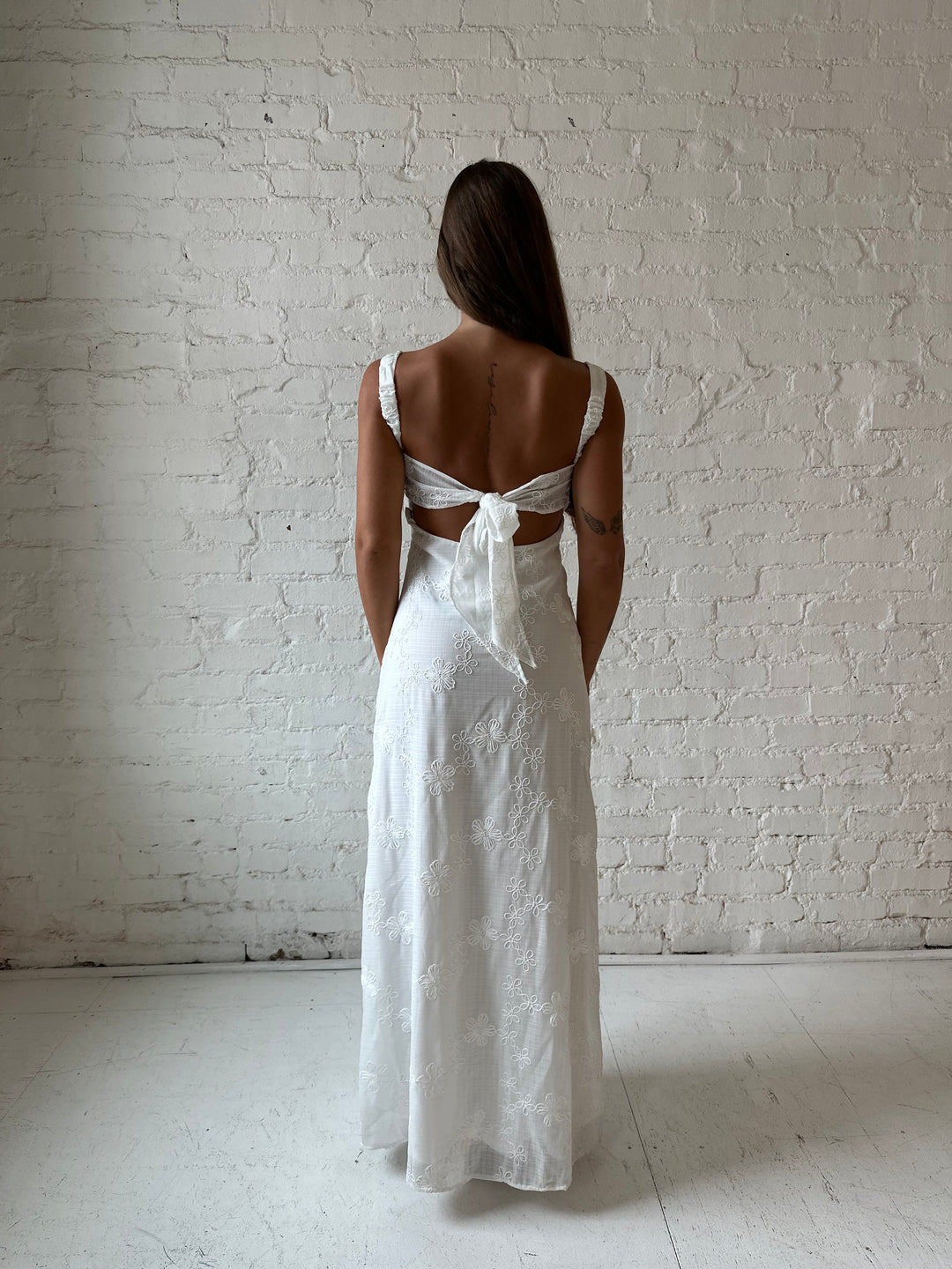 Woman wearing white embroidered maxi dress with sweetheart neckline, and tie back.