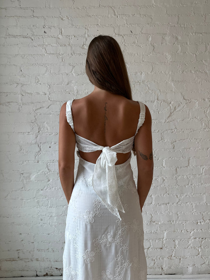 Woman wearing white embroidered maxi dress with sweetheart neckline, and tie back.
