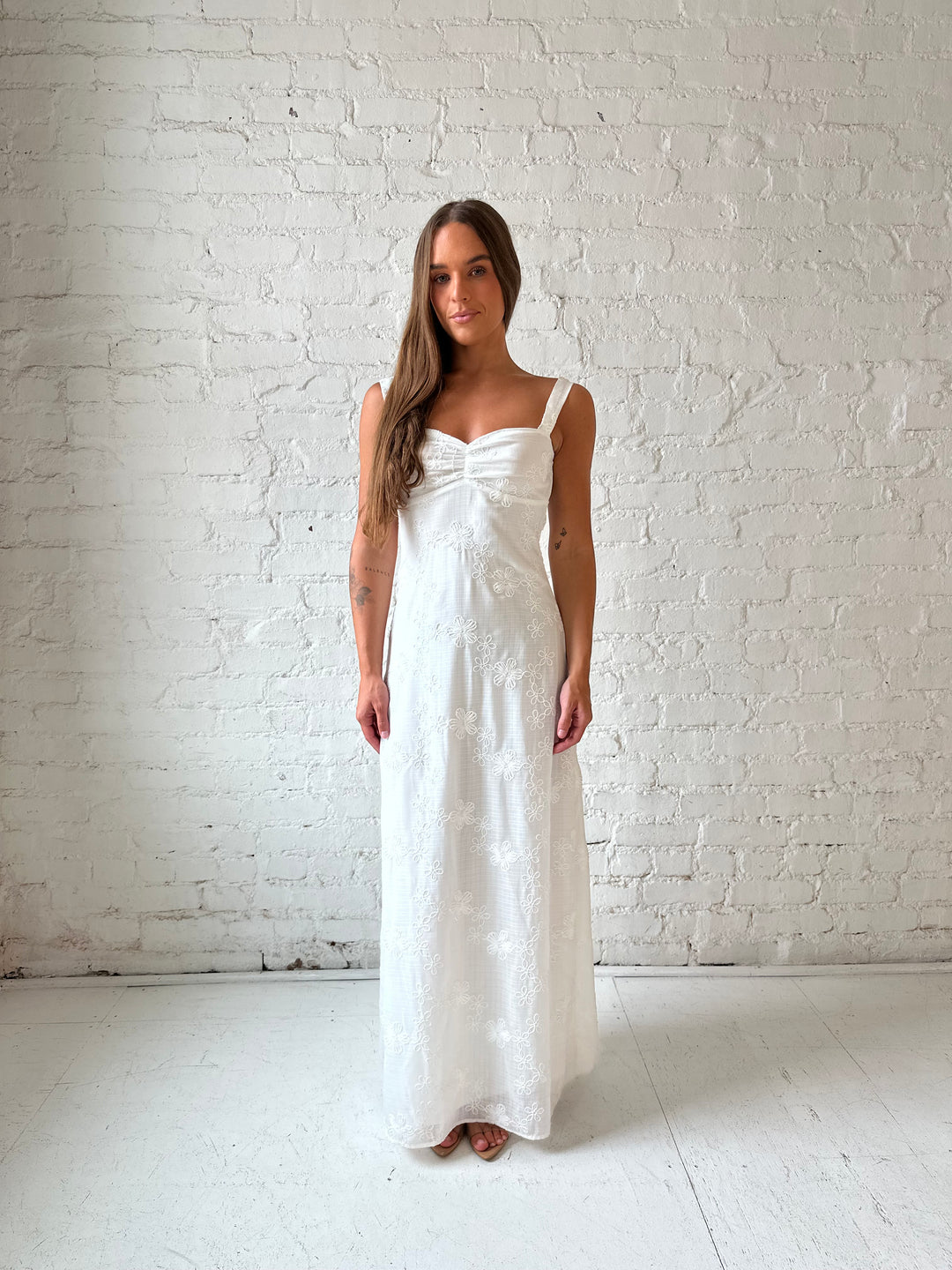 Woman wearing white embroidered maxi dress with sweetheart neckline, and tie back.