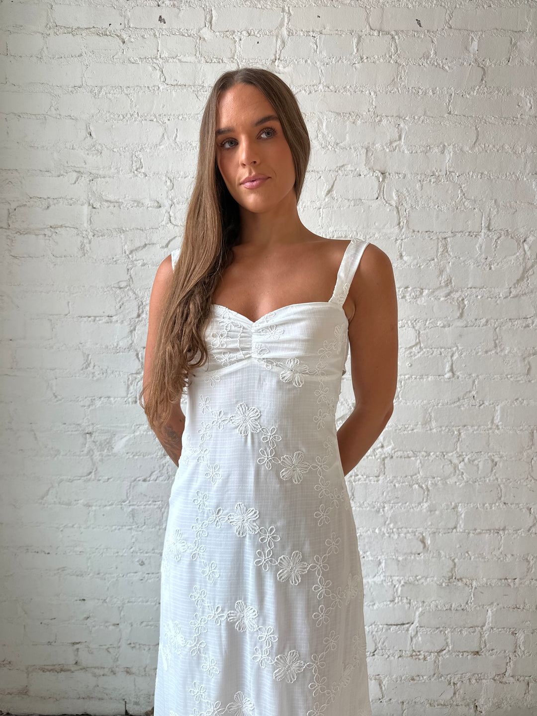 Woman wearing white embroidered maxi dress with sweetheart neckline, and tie back.
