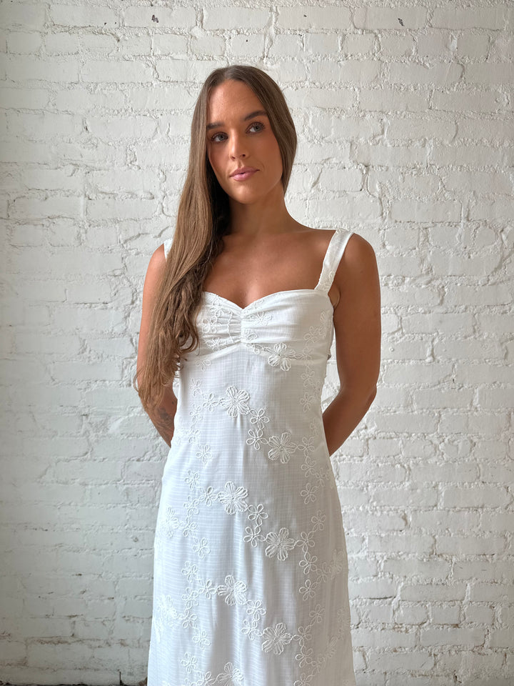 Woman wearing white embroidered maxi dress with sweetheart neckline, and tie back.