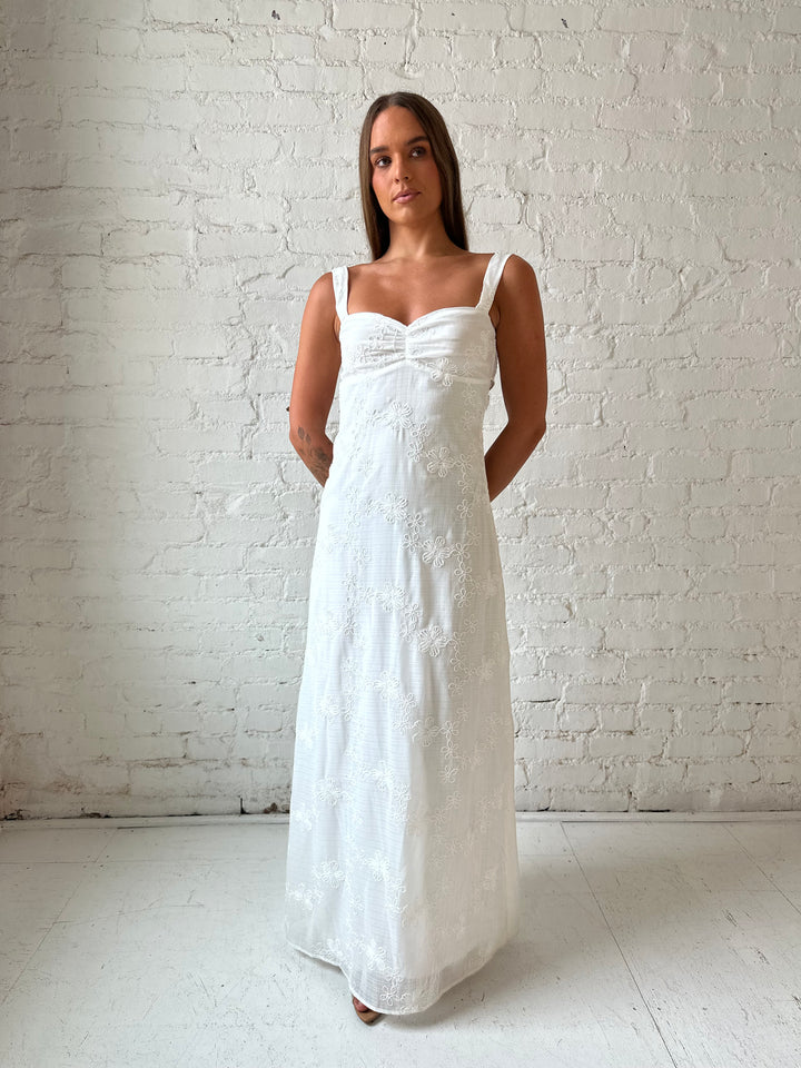 Woman wearing white embroidered maxi dress with sweetheart neckline, and tie back.