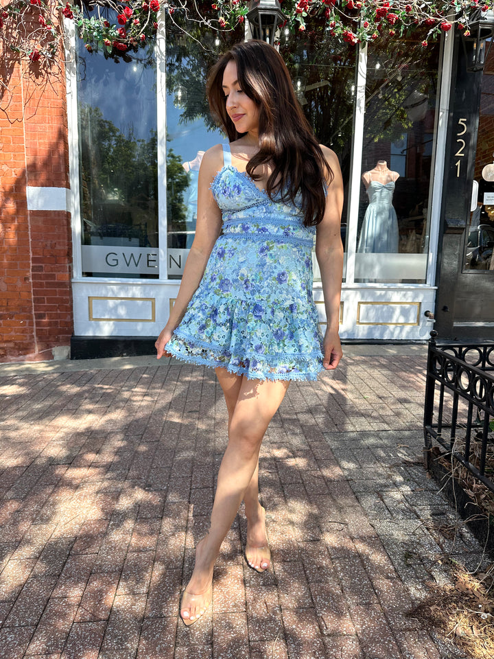 Woman wearing blue textured floral mini dress with tiered bottom, and adjustable straps.