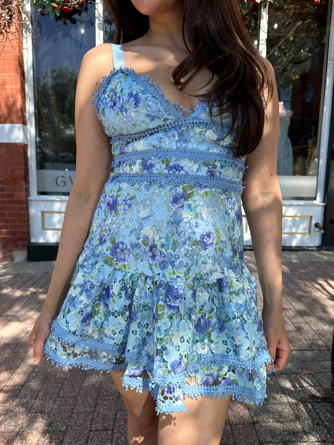 Woman wearing blue textured floral mini dress with tiered bottom, and adjustable straps.