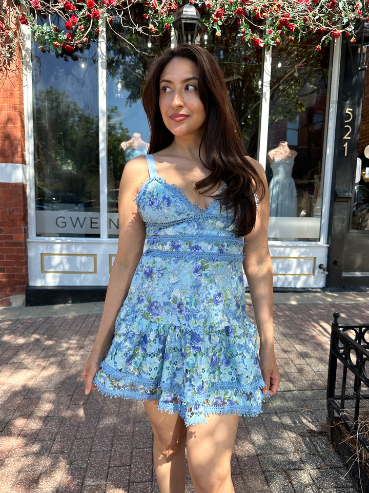 Woman wearing blue textured floral mini dress with tiered bottom, and adjustable straps.