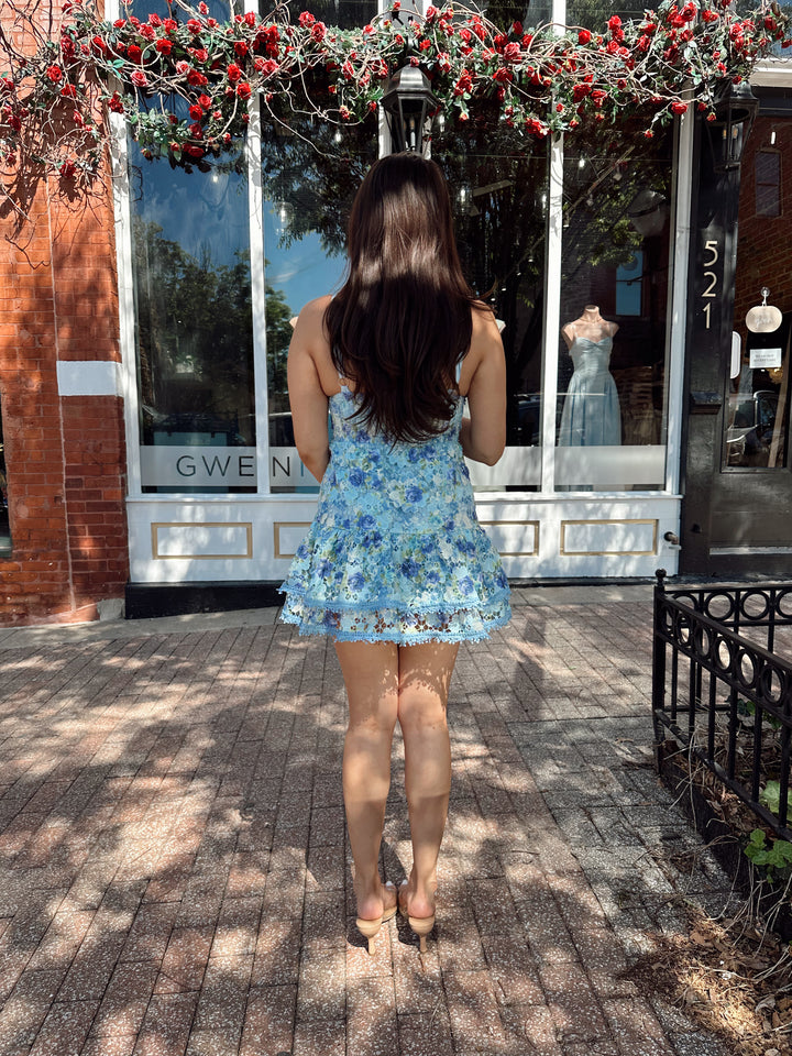Woman wearing blue textured floral mini dress with tiered bottom, and adjustable straps.