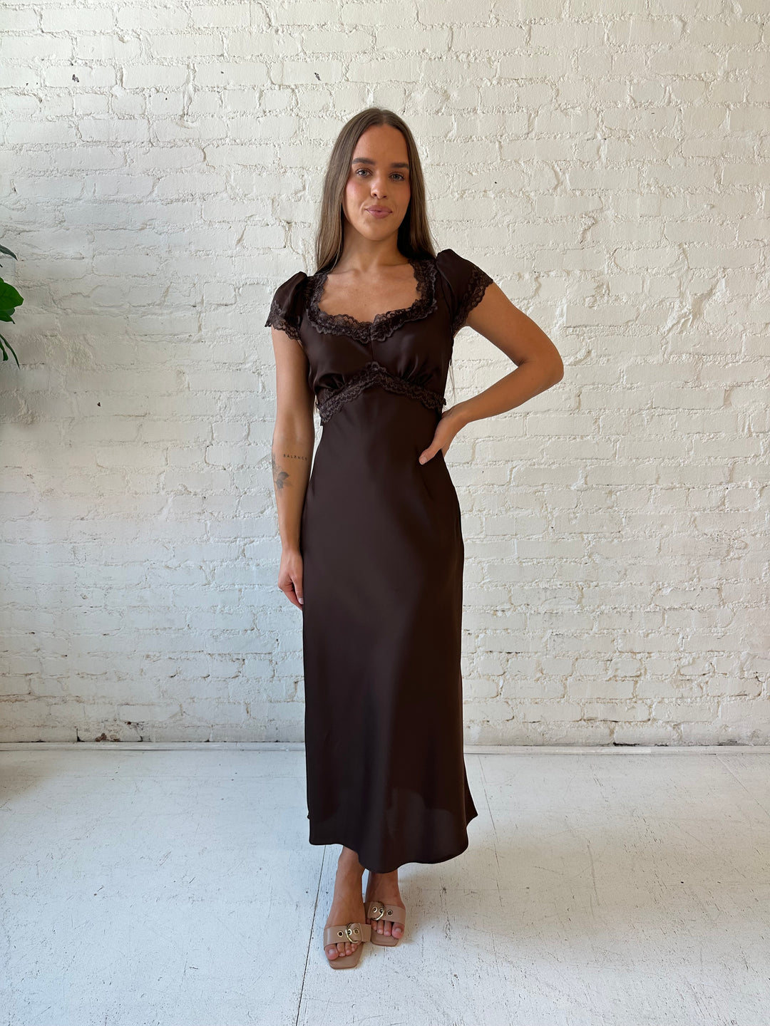 Woman wearing dark brown satin maxi dress with lace trim detailing and flutter sleeves. 