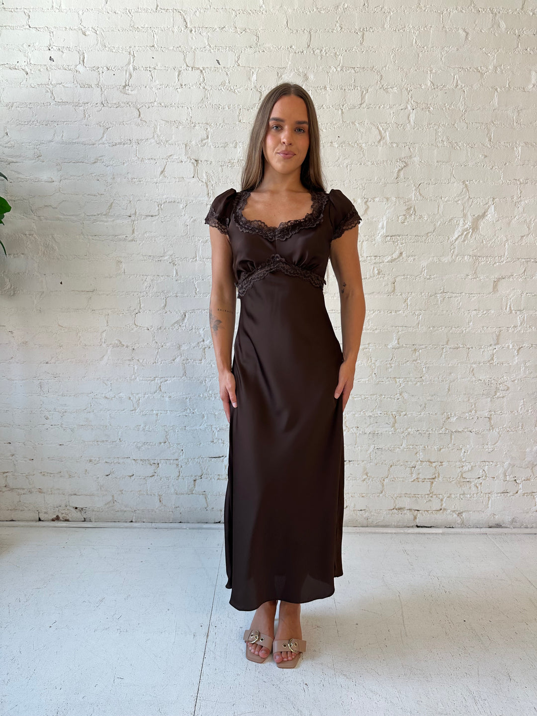 Woman wearing dark brown satin maxi dress with lace trim detailing and flutter sleeves. 