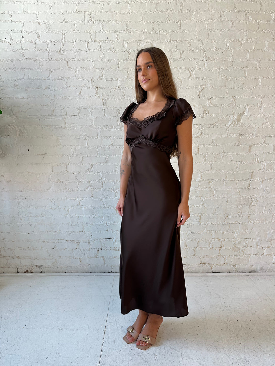 Woman wearing dark brown satin maxi dress with lace trim detailing and flutter sleeves. 