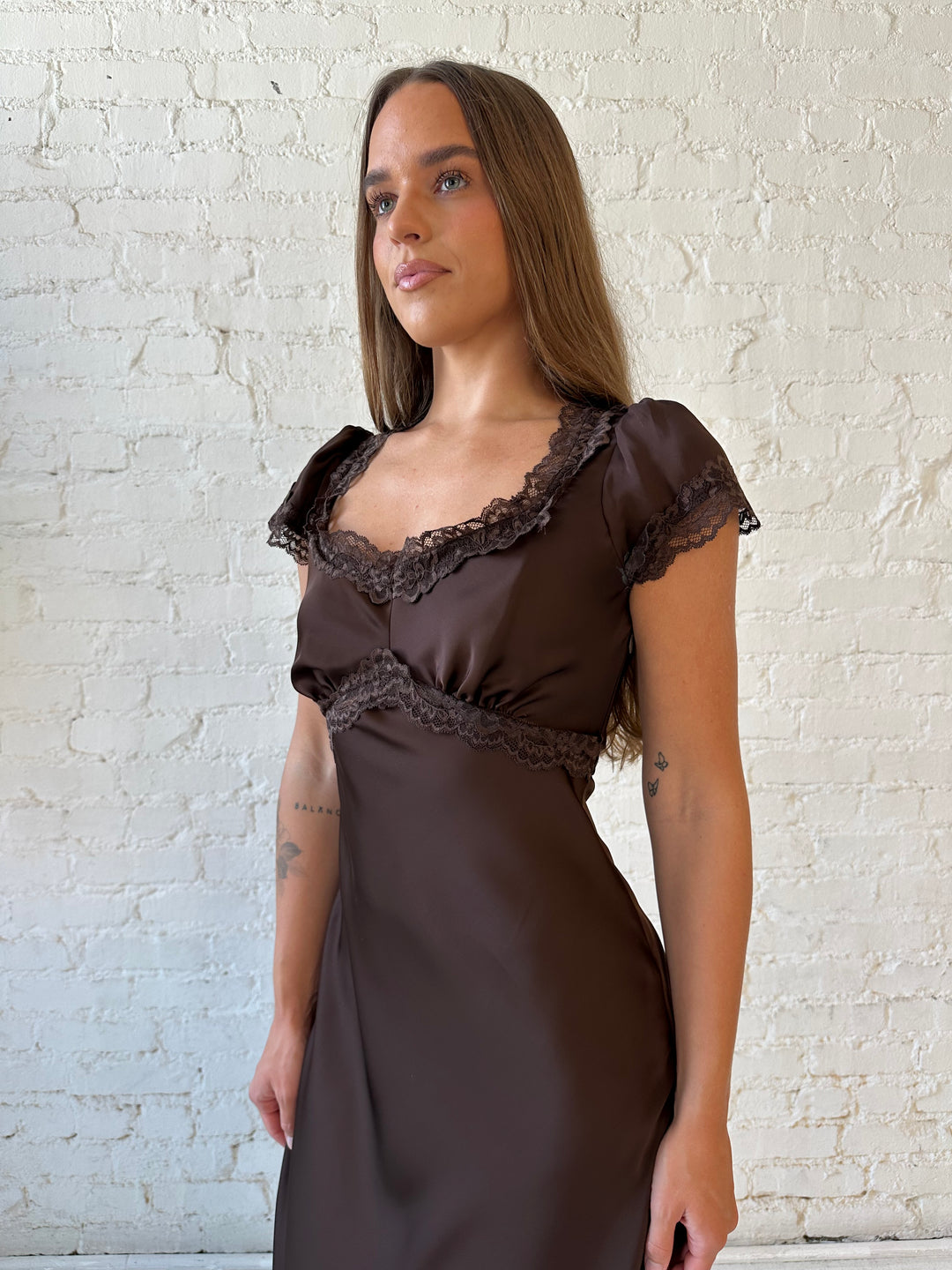 Woman wearing dark brown satin maxi dress with lace trim detailing and flutter sleeves. 
