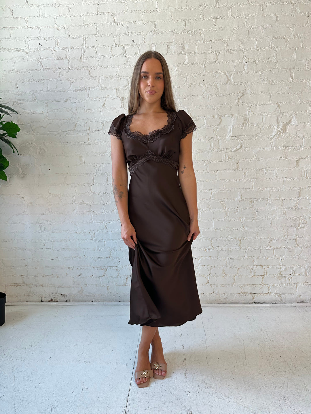 Woman wearing dark brown satin maxi dress with lace trim detailing and flutter sleeves. 