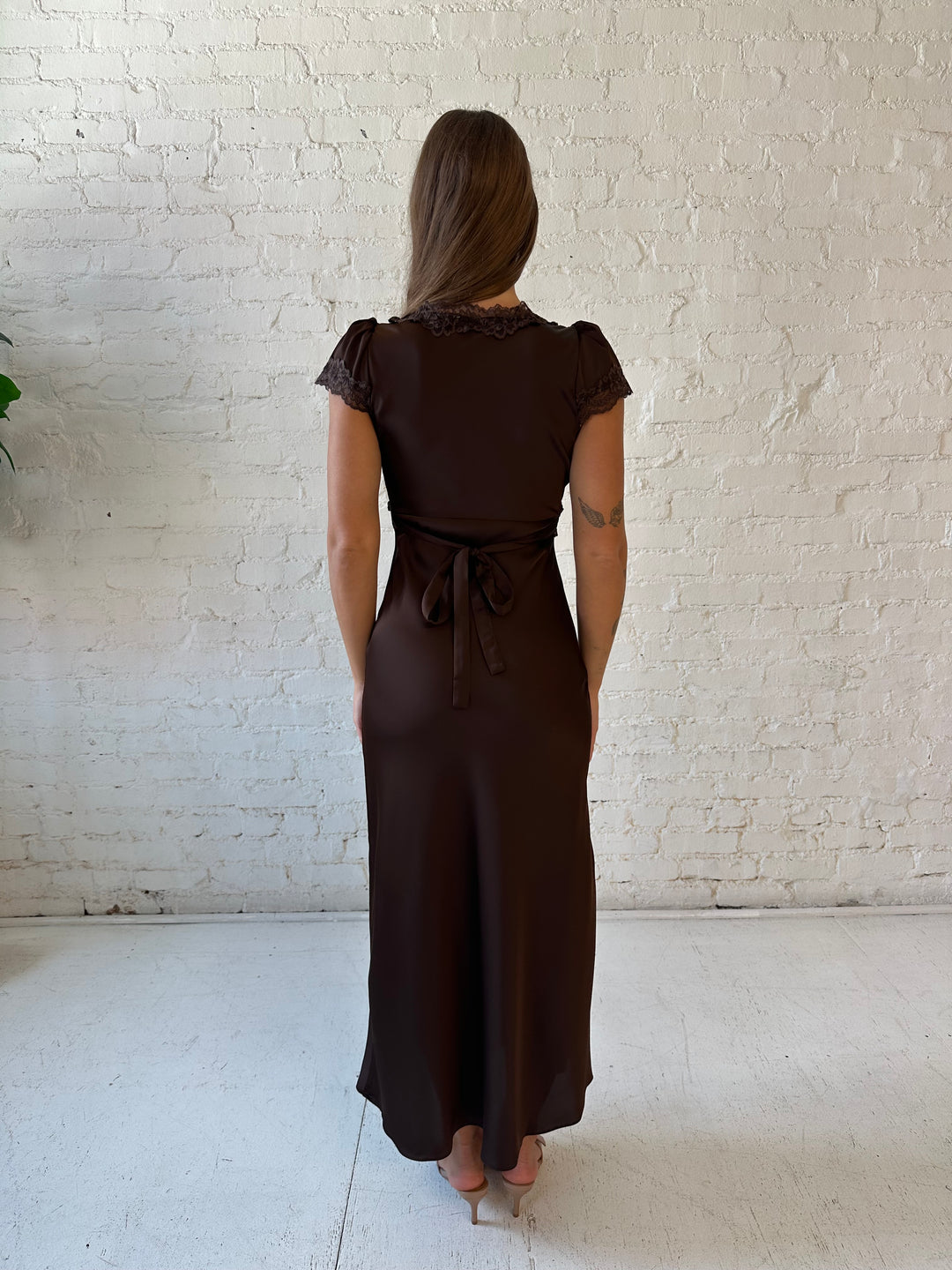 Woman wearing dark brown satin maxi dress with lace trim detailing and flutter sleeves. 