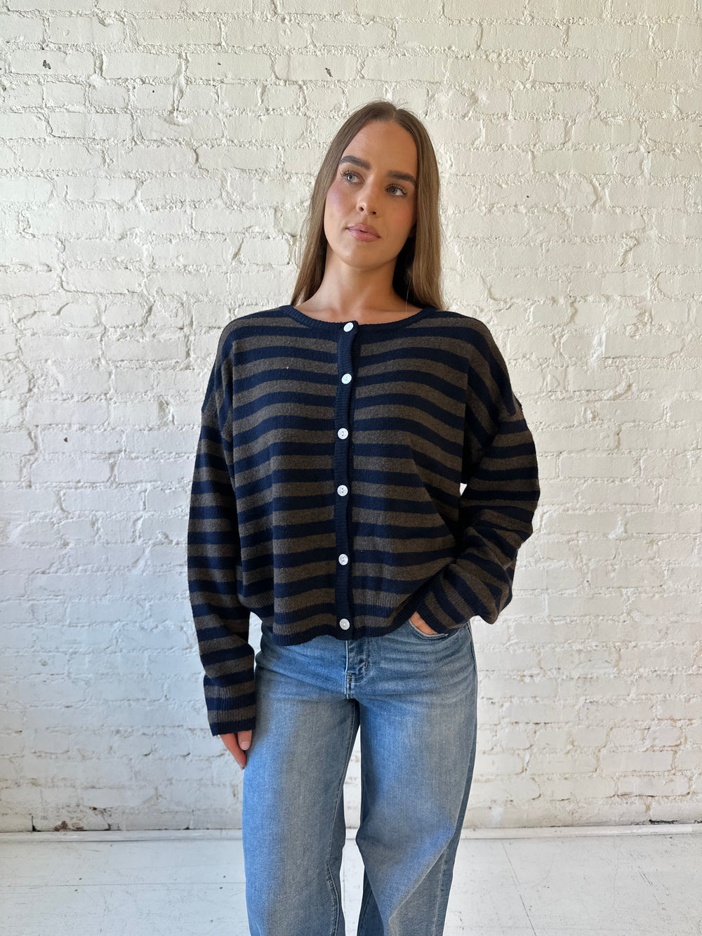 Woman wearing navy and taupe striped button down cardigan with medium wash jeans.