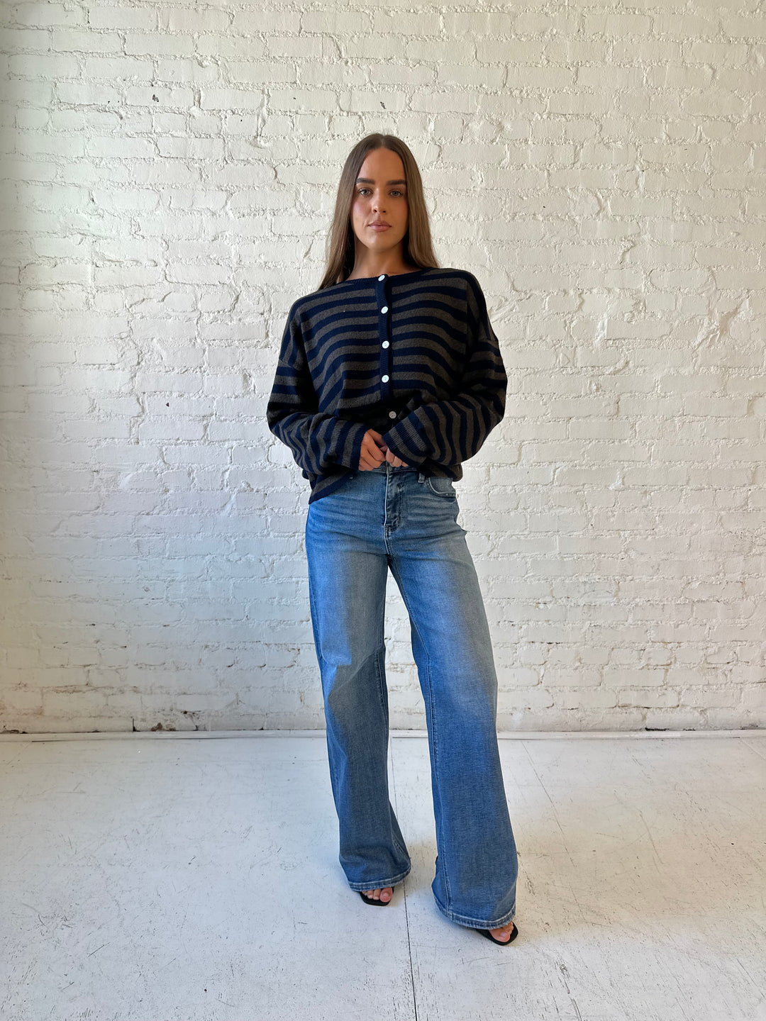 Woman wearing navy and taupe striped button down cardigan with medium wash jeans.