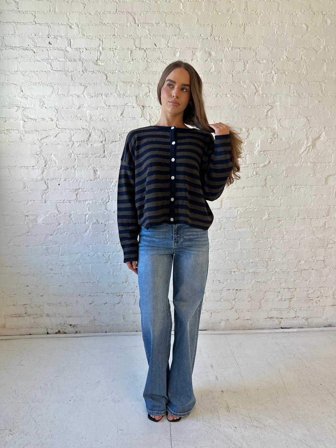 Woman wearing navy and taupe striped button down cardigan with medium wash jeans.