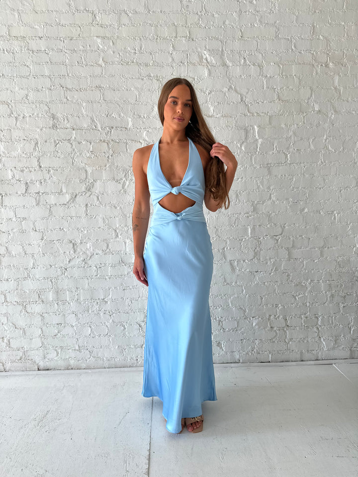 Woman wearing light blue maxi dress with halter neckline and twist cutout midsection. 