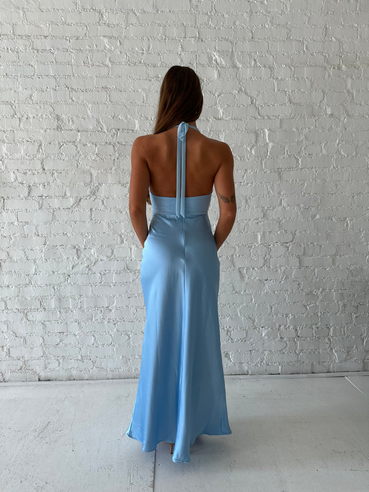Woman wearing light blue maxi dress with halter neckline and twist cutout midsection. 
