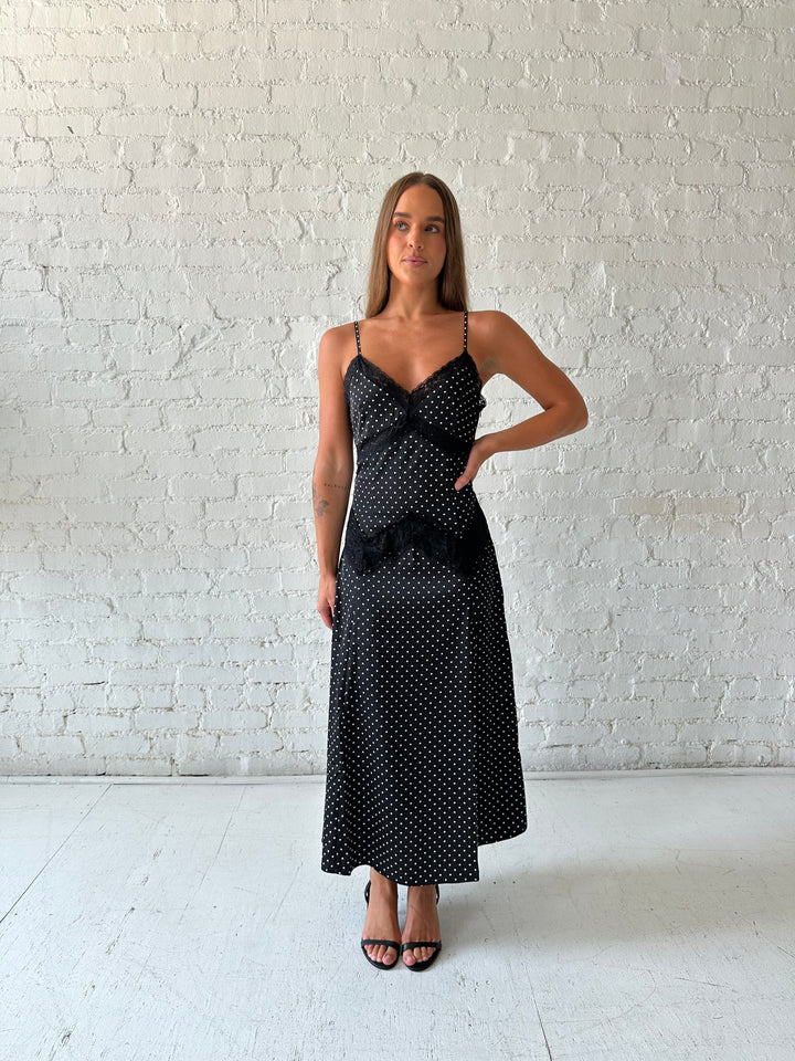 Woman wearing black polka dot satin maxi dress with lace trim detail.