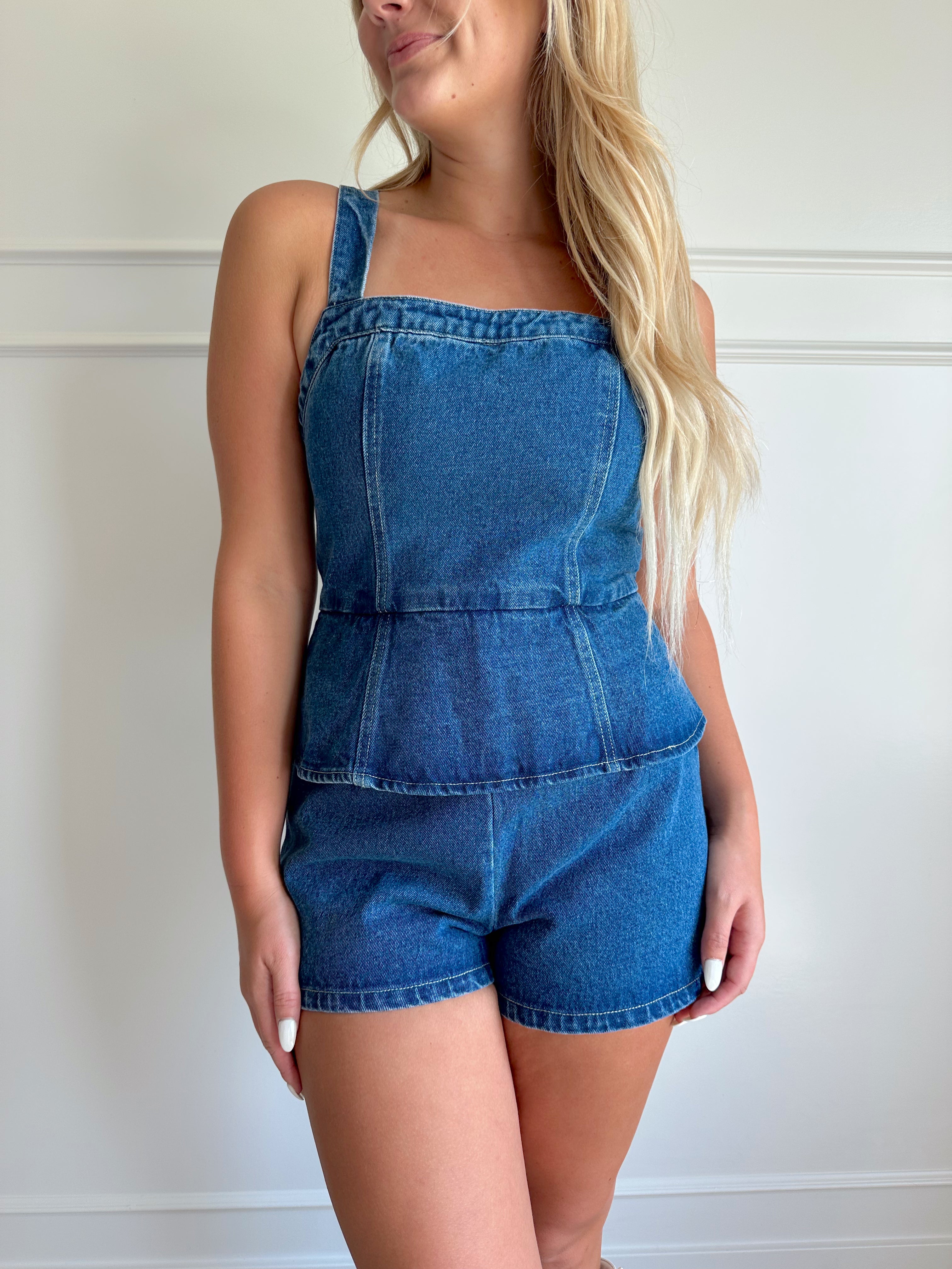 Dark wash denim peplum romper with self tie back closure.